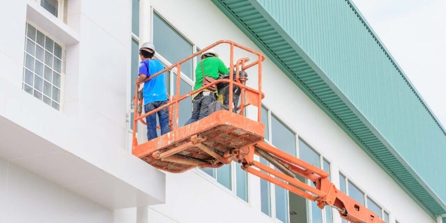 Worker man on a Scissor hydraulic Lift table Platform towards a factory roof at a construction site