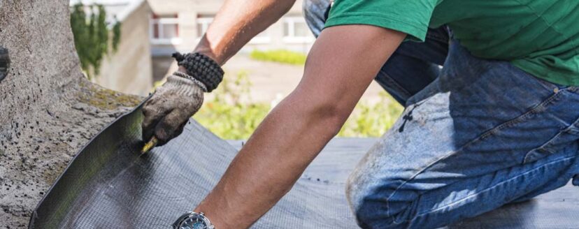 A construction worker cuts waterproofing material and prepares it for installation. Overhaul of the roof of the house.