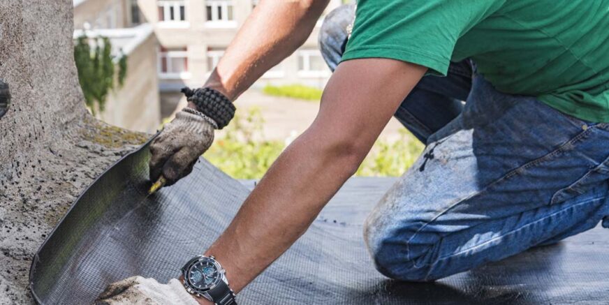 A construction worker cuts waterproofing material and prepares it for installation. Overhaul of the roof of the house.